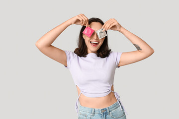 Funny young woman with condoms on grey background. Safe sex concept