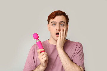 Shocked young man with vibrator on grey background
