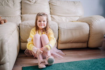 A little girl is sitting on the ground by a white leather sofa