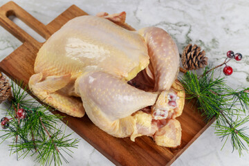 Raw whole chicken is being prepared for Christmas dinner on wooden board.