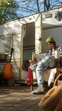 A beautiful hippie girl illustrating on a tablet while sitting in front of the trailer in the autumn garden.