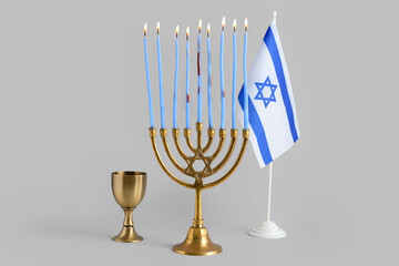 Menorah with burning candles, cup and flag of Israel for Hanukkah celebration on grey background