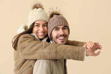Loving couple in winter clothes hugging on beige background