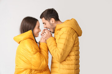 Loving couple in winter clothes warming hands on light background