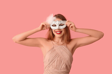 Happy young woman in white carnival mask on pink background