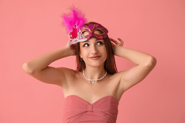 Beautiful young woman in carnival mask on pink background