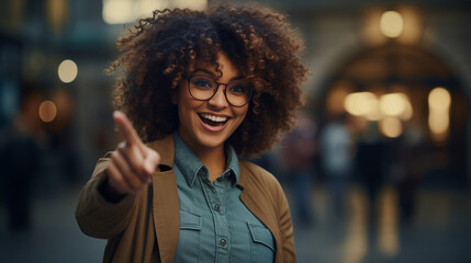 Woman with stylish outfit afro hair and glasses smiling pointing with finger at copy space