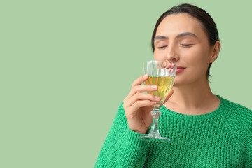 Beautiful young woman with glass of white wine on green background