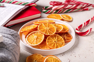 Plate with dried orange slices and Christmas candy canes on white background