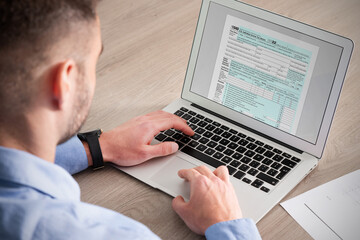 Man filling tax form with laptop - obrazy, fototapety, plakaty