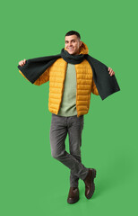 Young man in yellow stylish puffer jacket and scarf on green background