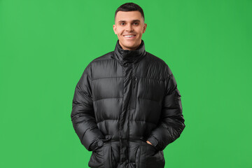 Young man in black stylish puffer jacket on green background