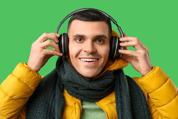 Young man in yellow stylish puffer jacket and headphones on green background