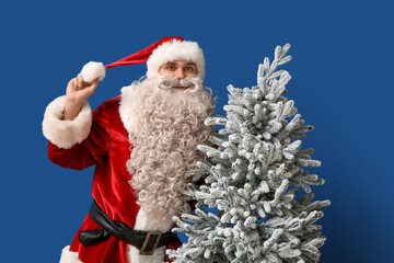 Young man in Santa Claus costume with white Christmas tree on blue background