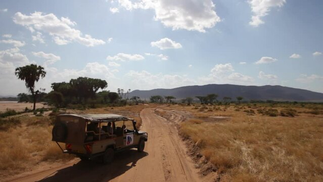 High, wide shot on safari vehicle driving on dirt road