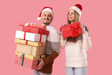Happy young couple in Santa hats with Christmas presents on pink background