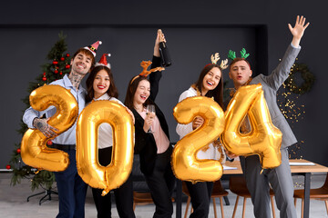 Young colleagues with figure 2024 and champagne celebrating New Year at corporate party in office