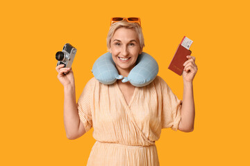 Mature woman with photo camera and passport on yellow background. Travel concept