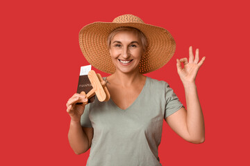 Mature woman with passport and wooden airplane showing OK on red background. Travel concept