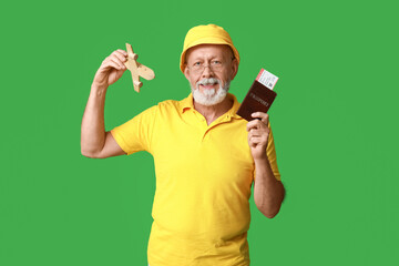 Mature male traveler with passport and wooden airplane on green background