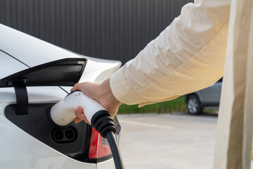 Young woman put EV charger to recharge electric car's battery from charging station. Alternative...