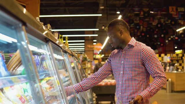 Black man shopping cheese in grocery store. A man chooses the French cheese brie or camembert