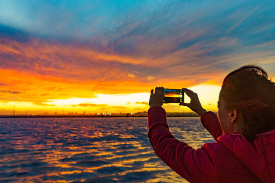 Woman photographing sunset over sea with mobile phone