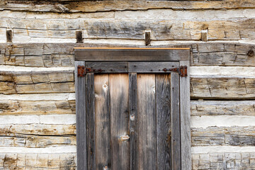 The wall of a log cabin, and an old window with hinges on the shutters. 
