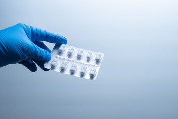 hand with blue gloves showing packaged white pills