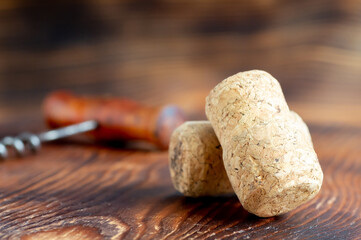 Two wine corks close-up, with a corkscrew in the background, on a wooden background