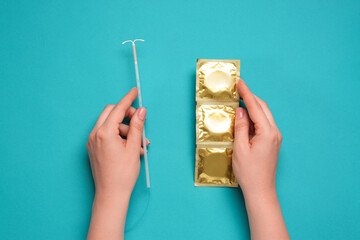 Woman with condoms and intrauterine device on light blue background, top view. Choosing birth control method - obrazy, fototapety, plakaty