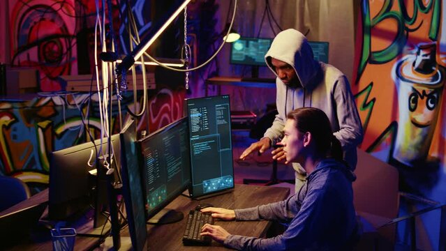 Hackers in underground hideout discussing ways to best hide their online activity through VPN and other methods after stealing data from victims, trying to avoid being detected by cybercrime police