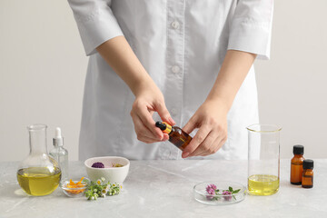 Scientist developing cosmetic oil at light grey table, closeup