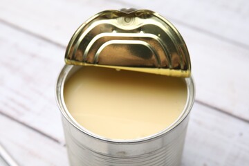 Tasty condensed milk in tin can on white wooden table, closeup