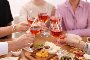 People clinking glasses with rose wine above table indoors, closeup