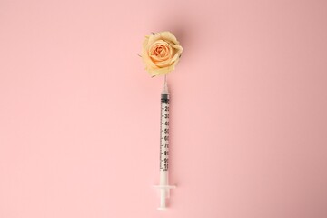 Medical syringe and beautiful rose on light pink background, top view