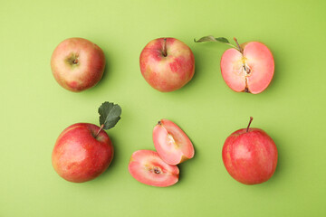 Tasty apples with red pulp and leaves on light green background, flat lay