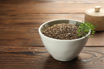 Bowl of dry seeds and fresh dill on wooden table, closeup. Space for text