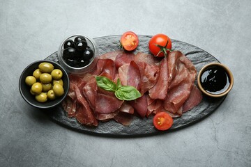 Delicious bresaola, tomato, olives and basil leaves on grey textured table, top view