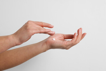 Woman applying cosmetic cream onto hand on white background, closeup