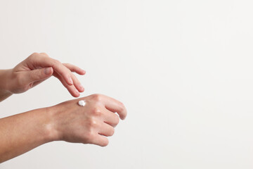 Woman applying cosmetic cream onto hand on white background, closeup. Space for text