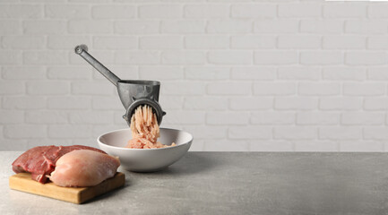 Manual meat grinder with mince, raw chicken and beef on grey table. Banner design with space for...