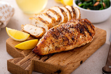 Grilled chicken breast whole and sliced on a cutting board with lemon - obrazy, fototapety, plakaty