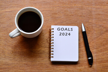 Goals 2024 text on notepad with coffee and pen on wooden desk.