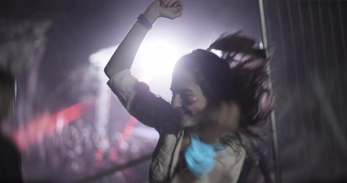 One girl dancing on a party with flashing lights and lasers. Out of focus crowd and dj stage in the background.