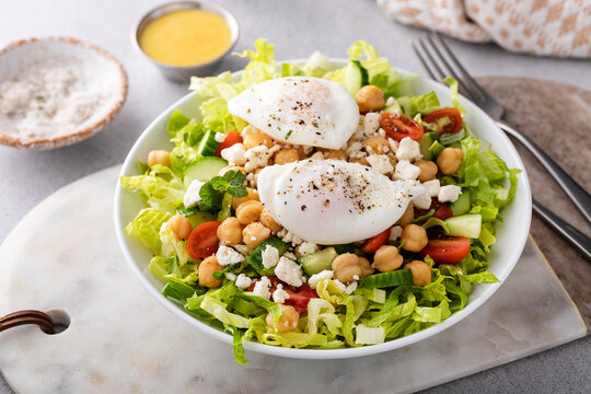 Healthy salad for lunch with fresh vegetables, chickpeas and feta topped with poached eggs