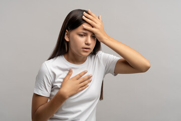 Teen girl feeling headache nausea touching chest forehead isolated on gray background. Teenager...