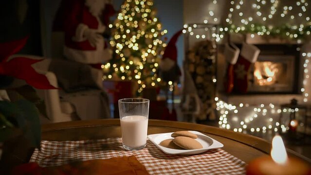 Santa Claus bringing gifts, eating ginger cookies and drinking milk on Christmas night in the decorated living room with fireplace and Christmas tree