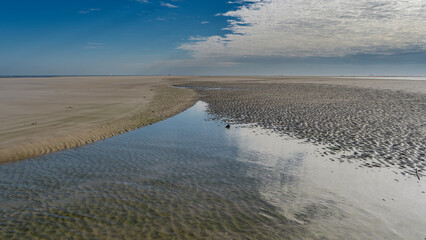 Low tide on the ocean. The seabed with undulating sandy ridges is exposed. The blue sky and clouds are reflected in a puddle of water. Madagascar. Morondava.