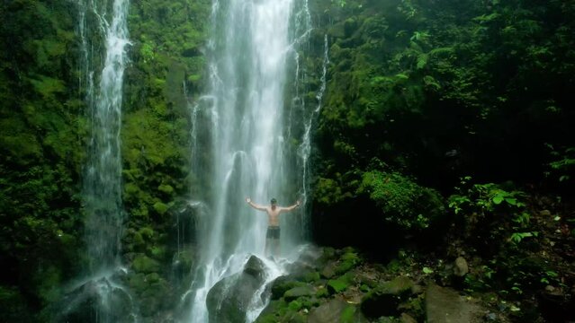 aerial view of a standing man spreading his arms under a waterfall